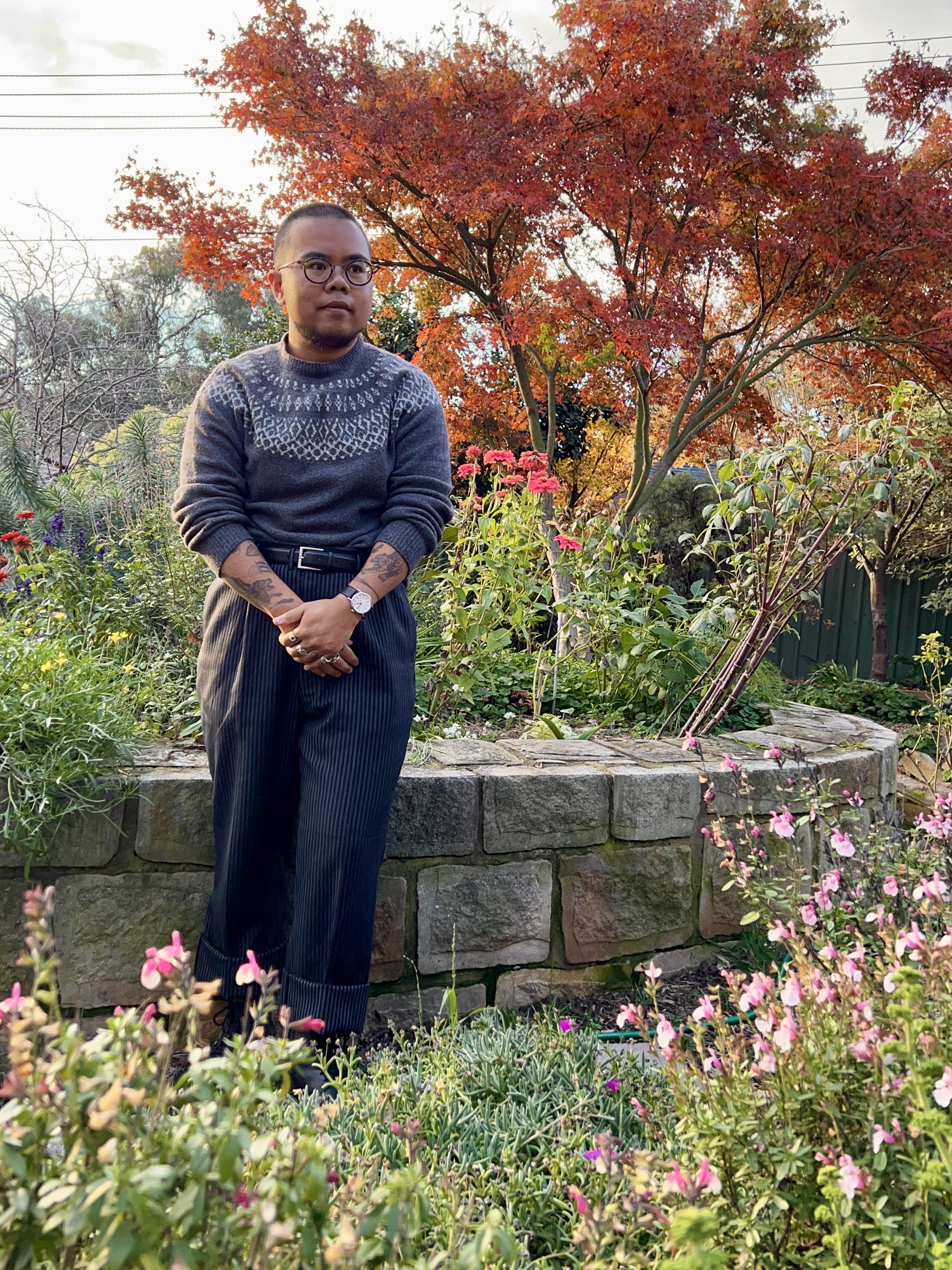 A photograph of a brown man standing in a garden in front of a Japanese maple.